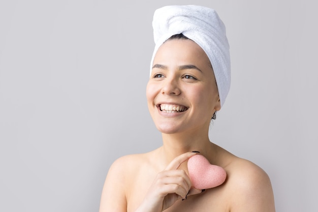 Ritratto di bellezza della donna in asciugamano bianco sulla testa con una spugna per un corpo in vista di un cuore rosa