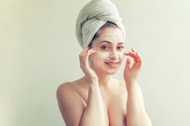 Ritratto di bellezza della donna in asciugamano sulla testa con maschera nutriente bianca o crema sul viso, sfondo bianco isolato. Cura della pelle pulizia eco cosmetici biologici spa relax concept