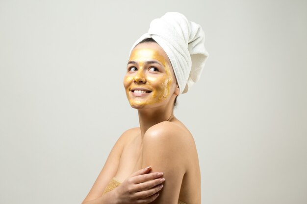 Ritratto di bellezza di donna in asciugamano bianco sulla testa con maschera nutriente dorata sul viso Cura della pelle