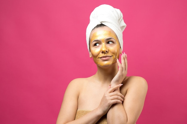 Ritratto di bellezza di donna in asciugamano bianco sulla testa con maschera nutriente dorata sul viso Pulizia della pelle eco-cosmetico biologico spa relax concept