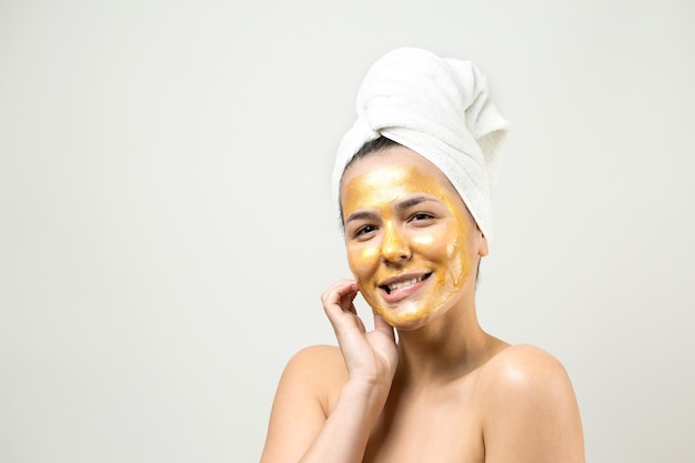 Ritratto di bellezza di donna in asciugamano bianco sulla testa con maschera nutriente dorata sul viso Pulizia della pelle eco-cosmetico biologico spa relax concept