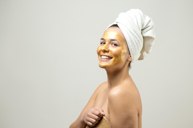 Ritratto di bellezza di donna in asciugamano bianco sulla testa con maschera nutriente dorata sul viso Pulizia della pelle eco-cosmetico biologico spa relax concept