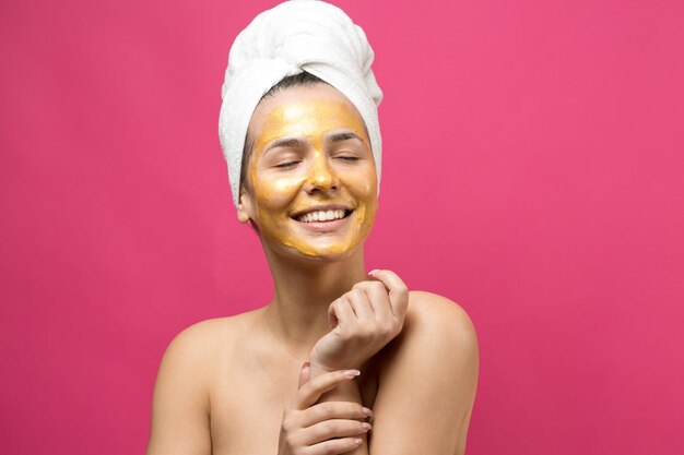 Ritratto di bellezza di donna in asciugamano bianco sulla testa con maschera nutriente dorata sul viso Pulizia della pelle eco-cosmetico biologico spa relax concept