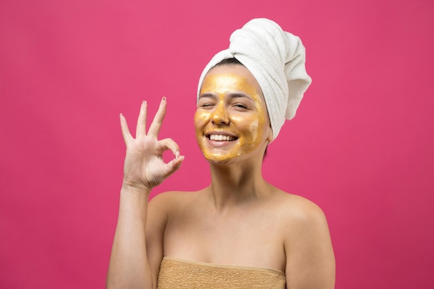 Ritratto di bellezza di donna in asciugamano bianco sulla testa con maschera nutriente dorata sul viso