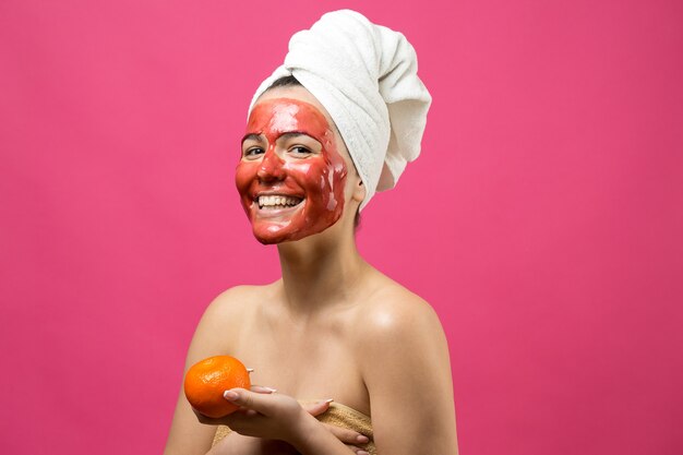 Ritratto di bellezza di donna in asciugamano bianco sulla testa con maschera nutriente rossa sul viso