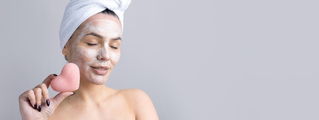 Ritratto di bellezza di donna in asciugamano bianco sulla testa con una spugna per un corpo in vista di un cuore rosa Skincare cleansing eco cosmetici organici spa relax concept