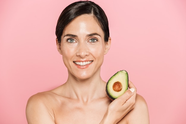 Ritratto di bellezza di una donna castana in topless sana sorridente attraente isolata, mostrando avocado affettato