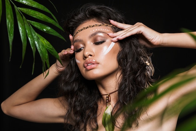 Ritratto di bellezza di una giovane donna bruna sensuale attraente che indossa accessori tribali in posa con foglie tropicali isolate