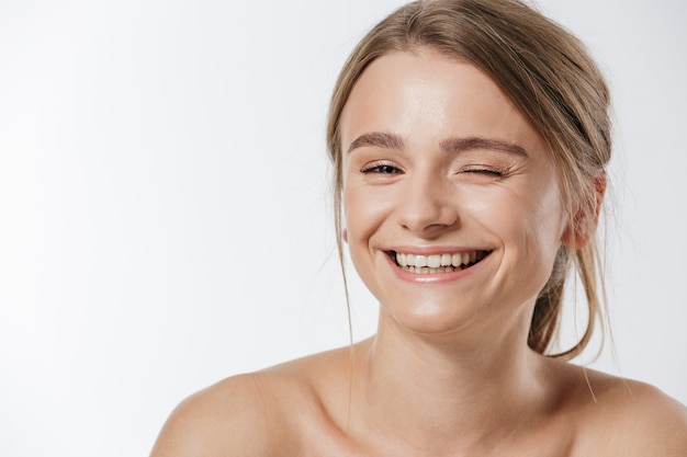 Ritratto di bellezza di una splendida giovane donna bionda seminuda con i capelli legati che strizzano l'occhio alla telecamera isolata su bianco