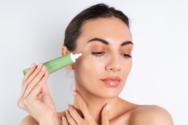 Ritratto di bellezza ravvicinato di una donna in topless con una pelle perfetta e un trucco naturale che tiene una crema per l'idratazione e l'elasticità della pelle sotto gli occhix9