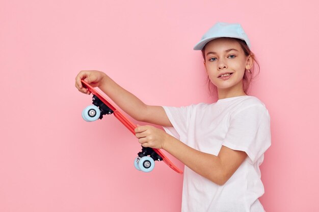 Ritratto di berretto ragazza bambino sorridente felice in maglietta bianca skateboard sfondo rosa