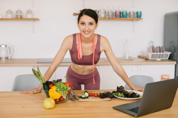 Ritratto di blogger donna sportiva che conduce una videoconferenza su un'alimentazione sana sul computer portatile in cucina