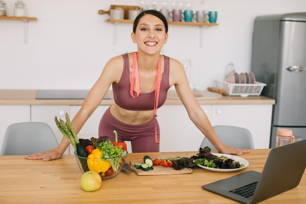 Ritratto di blogger donna sportiva che conduce una videoconferenza su un'alimentazione sana sul computer portatile in cucina