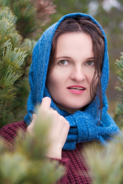 Ritratto di bruna in piedi nella foresta di pini. Donna vestita con maglione marrone, sciarpa blu gettata sulla testa