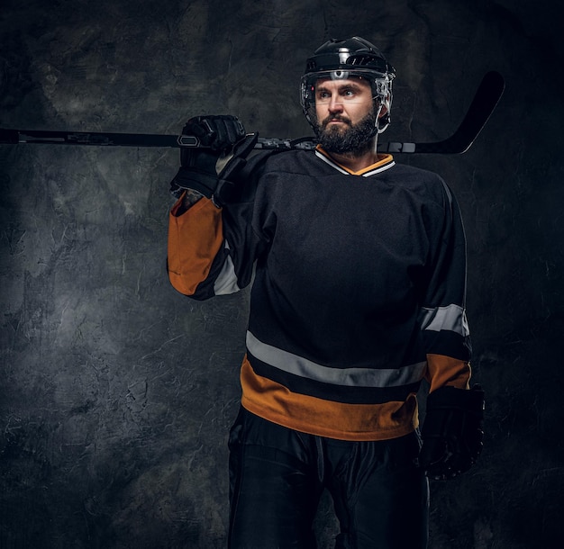 Ritratto di brutale uomo barbuto in uniforme da giocatore di hockey in studio fotografico scuro.