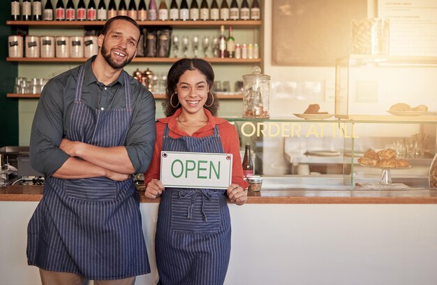 Ritratto di caffè o coppia felice con un cartello aperto per accogliere le vendite con ospitalità in un bar Partnership di manager o imprenditori sorridono in piedi con un cartellone pubblicitario o di apertura in negozio