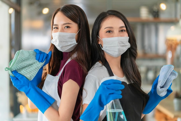 Ritratto di cameriera asiatica con personale grembiule che indossa protezione guanto di gomma protezione maschera protezione mano asciugamano per la pulizia e disinfettante spray alcolico per proteggere l'infezione idee per la salute del coronavirus