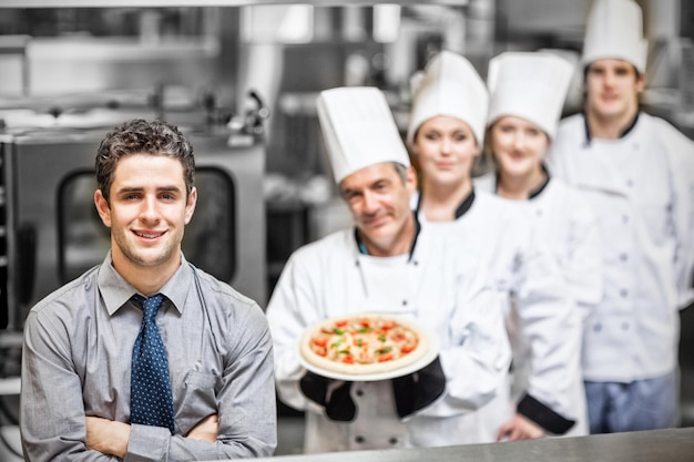 Ritratto di cameriere in piedi davanti a chef che tengono la pizza in cucina professionale