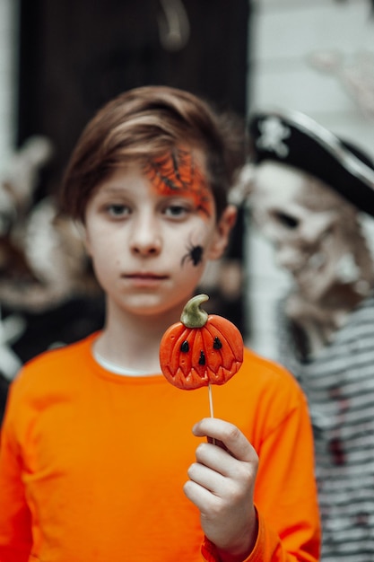 Ritratto di candido ragazzo adolescente autentico con la faccia dipinta alla festa di Halloween con Jack lollipop