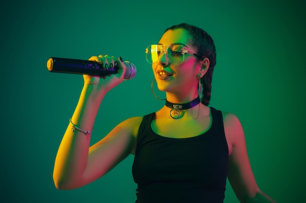 Ritratto di cantante femminile caucasico isolato su sfondo verde studio in luce al neon