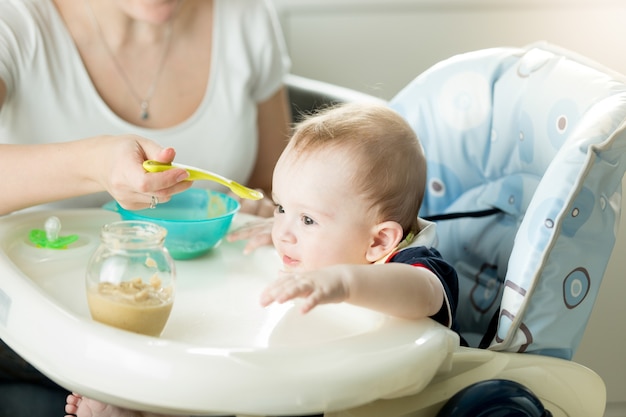 Ritratto di carino adorabilmente bambino seduto su una sedia e mangiare dal cucchiaio