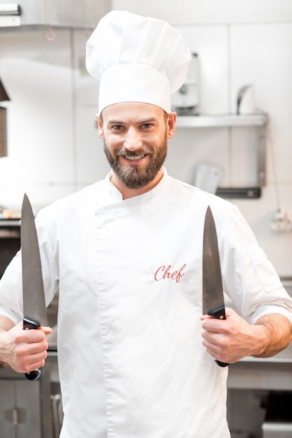 Ritratto di chef cuoco in uniforme con coltelli nella cucina del ristorante