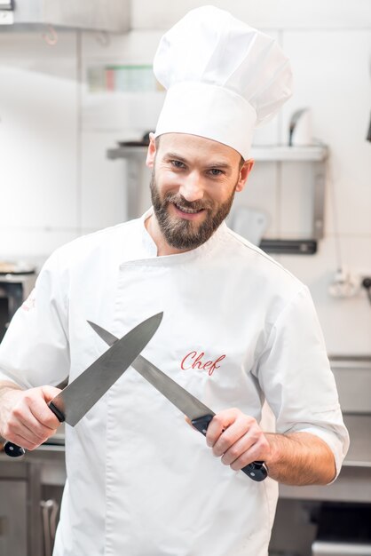 Ritratto di chef cuoco in uniforme con coltelli nella cucina del ristorante