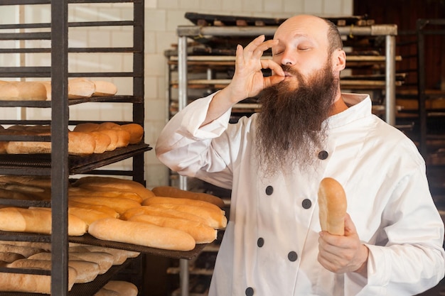 Ritratto di chef maschio adulto professionista con barba lunga in uniforme bianca in piedi nel suo posto di lavoro e cuoco con gesto di approvazione del gusto che mostra segno perfetto Concetto di professione interna occhi chiusi