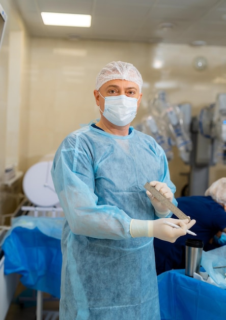 Ritratto di chirurgo maschile in sala operatoria che guarda la fotocamera Dottore in scrub e maschera medica nella moderna sala operatoria dell'ospedale