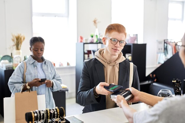 Ritratto di cliente maschio sorridente che paga nel negozio di abbigliamento tramite lo spazio di copia nfc dello smartphone