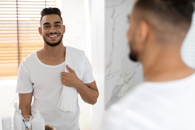 Ritratto di concetto di cura di sé dell'uomo arabo sorridente bello che posa nell'interno del bagno