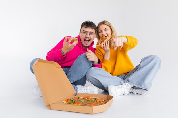 Ritratto di coppia allegra uomo e donna in maglioni colorati che sorridono mentre si mangia la pizza