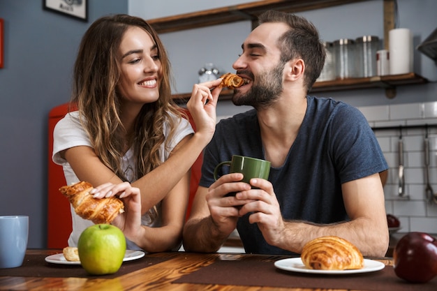 Ritratto di coppia europea uomo e donna che mangia croissant mentre si consuma la colazione in cucina elegante