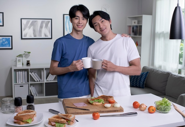 Ritratto di coppia gay asiatica romantica che cucina in cucina e guarda la fotocamera Le coppie di uomini lgbt si divertono insieme mentre preparano cibo sano Concetto di stile di vita sano