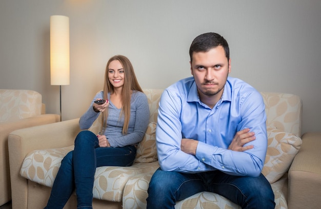 Ritratto di coppia seduta sul divano a guardare la televisione. Immagine di donna con telecomando in mano e uomini sconvolti