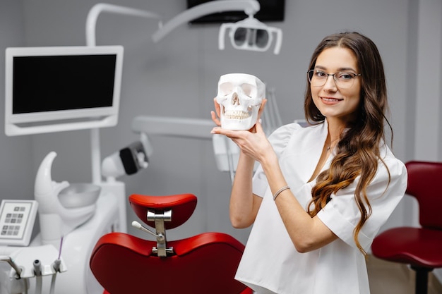 Ritratto di dentista femminile che tiene il modello del cranio e spiega le regole di igiene dei denti al paziente davanti alla macchina fotografica