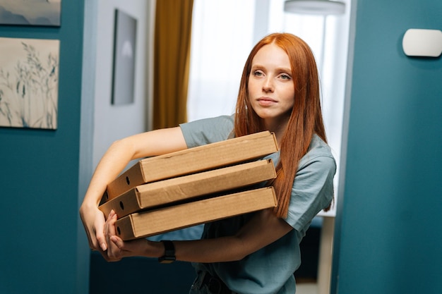 Ritratto di donna abbastanza giovane che tiene scatole di pizza calda in piedi a due passi dall'appartamento in attesa