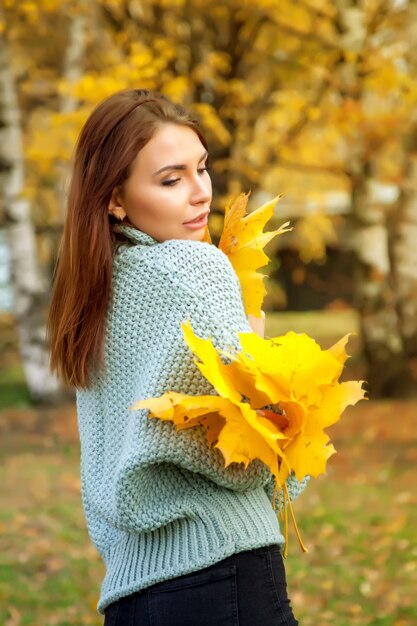 Ritratto di donna abbastanza giovane di aspetto slavo in abbigliamento casual in autunno, sta con le foglie in mano