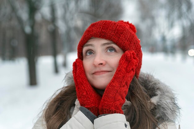 Ritratto di donna abbastanza giovane in cappello rosso e guanti sullo sfondo del parco invernale. Avvicinamento