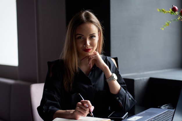 Ritratto di donna abbastanza giovane sorridente di affari che si siede sul posto di lavoro.