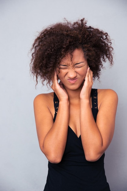 Ritratto di donna afro-americana che copre le sue orecchie oltre il muro grigio