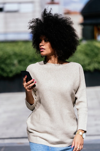 Ritratto di donna afro attraente utilizzando il telefono cellulare in strada. Concetto di donna d'affari