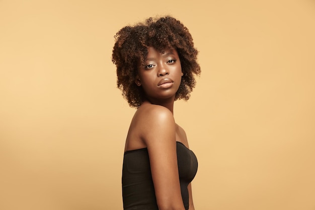 Ritratto di donna afroamericana attraente con capelli afro su sfondo beige isolato