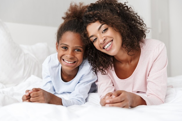 Ritratto di donna afroamericana e la sua piccola figlia che sorridono e si trovano a letto a casa
