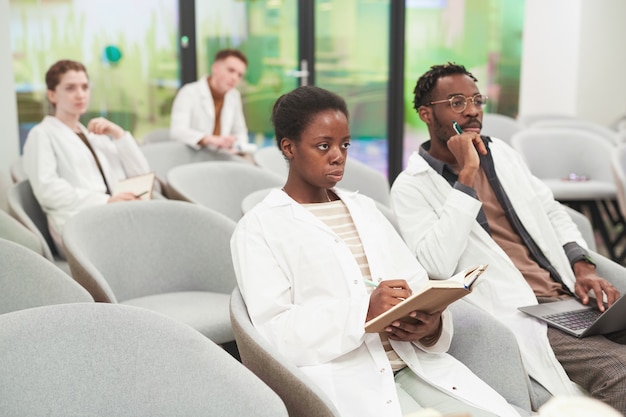 Ritratto di donna afroamericana seduta in pubblico con un gruppo multietnico di persone mentre ascolta una lezione di medicina, copia spazio