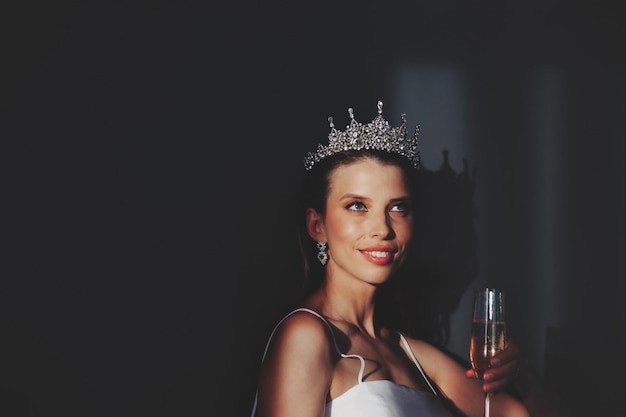 Ritratto di donna alla moda in corona con champagne sullo sfondo delle ombre nel soggiorno scuro che guarda in alto