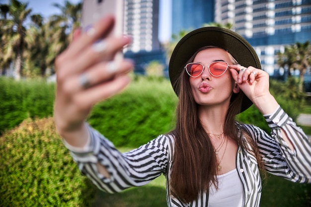 Ritratto di donna alla moda spensierata hipster indossando cappello di feltro e occhiali rosso brillante