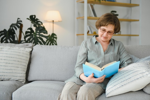 Ritratto di donna allegra focalizzata attraente seduta sul divano libro di lettura passatempo sognare ad occhi aperti a casa casa appartamento al coperto