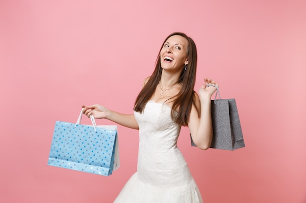 Ritratto di donna allegra in abito bianco che cerca con in mano pacchetti multicolori borse con acquisti dopo lo shopping