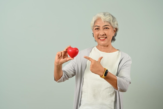 Ritratto di donna anziana attraente che tiene il cuore rosso nelle sue mani Persone anziane e concetto di assistenza sanitaria